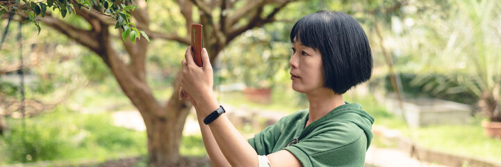 Asian mature woman take a picture at a fruit farm, banner of travel and technology concept