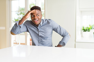 Handsome african american man on white table very happy and smiling looking far away with hand over...