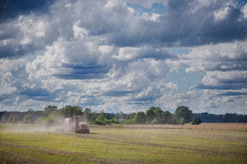 Obraz premium Agricultural background with red tractor pulling plow, throwing dust in air. Combine harvester at wheat field. Heavy machinery during cultivation, working on fields. Dramatic sky, rain, storm clouds 