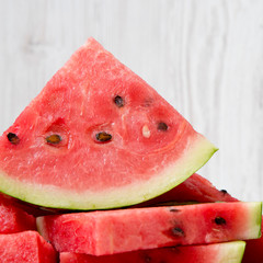 Chopped ripe juicy watermelon over white wooden background, side view.