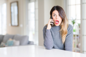 Young beautiful woman talking on the phone at home scared in shock with a surprise face, afraid and excited with fear expression