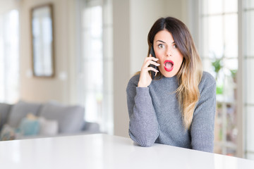 Fototapeta premium Young beautiful woman talking on the phone at home scared in shock with a surprise face, afraid and excited with fear expression