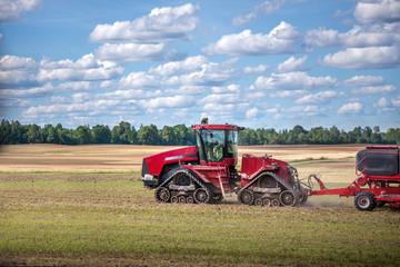 Obraz premium Agricultural background with red tractor pulling plow, throwing dust in air. Combine harvester at wheat field. Heavy machinery during cultivation, working on fields. Dramatic sky, rain, storm clouds 