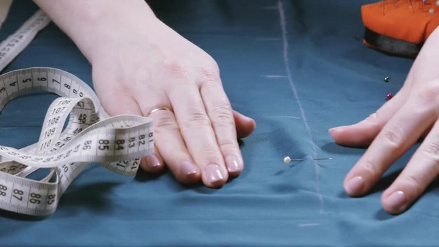 Seamstress at work with ruler measures piece of blue tissue on table in workshop close-up