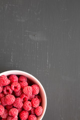Raw raspberries in a pink bowl on black background, top view. Healthy eating and dieting. From...