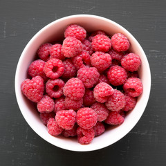Pink bowl of raspberry on black surface, top view. From above, overhead. Close-up.