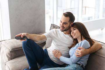 Image of european couple holding remote control while watching television in living room