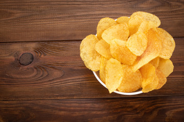 Crispy potato chips in bowl on wooden background. Top view with copyspace
