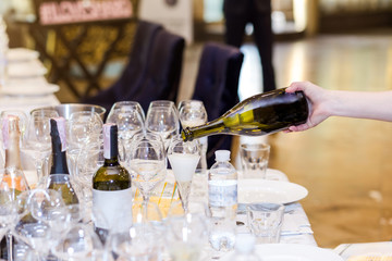 The waiter pours champagne into a glass on the white table