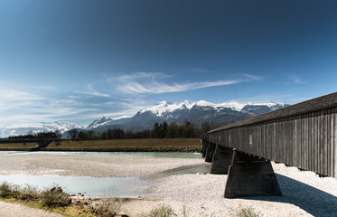 historic wooden covered bridge across the Rhine with mountain landscape and blue sky in the background
