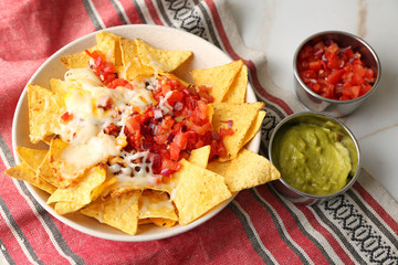 Plate with tasty nachos, cheese, minced meat and salsa on table