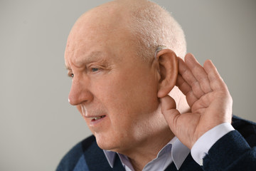 Senior man with hearing aid on light background