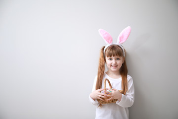 Cute little girl with Easter eggs and bunny ears on light background