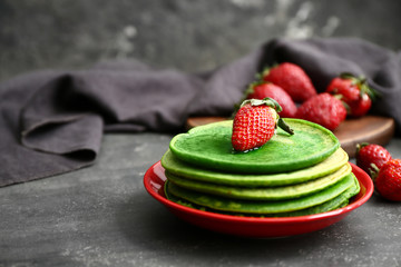 Plate with tasty green pancakes on dark background