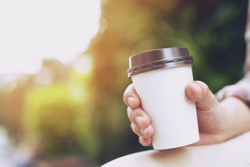 people business man hand holding paper cup of take away drinking coffee on natural morning sunlight sitting in public park. space Place for your text or logo.