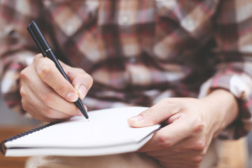 close up hand young man are sitting chair using pen writing Record Lecture notepad into the book