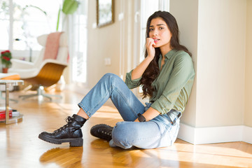 Young beautiful woman sitting on the floor at home looking stressed and nervous with hands on mouth biting nails. Anxiety problem.