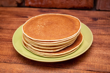 Stack of pancakes on the wooden background on the green dish