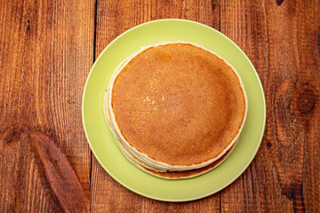 Stack of pancakes on the wooden background on the green dish