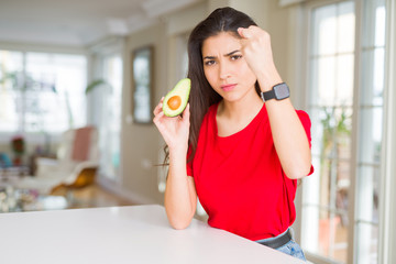 Young woman eating healthy avocado annoyed and frustrated shouting with anger, crazy and yelling with raised hand, anger concept