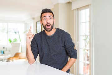 Fototapeta premium Handsome hispanic man wearing casual sweater at home pointing finger up with successful idea. Exited and happy. Number one.