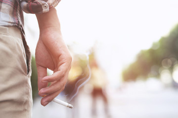 man holding smoking a cigarette in hand. Cigarette smoke spread in public areas outdoor. blur...