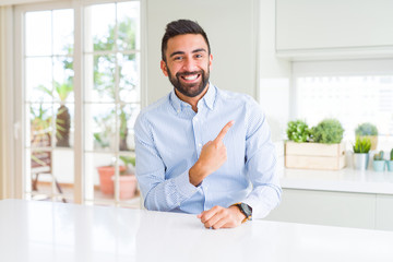 Handsome hispanic business man cheerful with a smile of face pointing with hand and finger up to the side with happy and natural expression on face