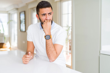 Fototapeta premium Handsome hispanic man casual white t-shirt at home looking stressed and nervous with hands on mouth biting nails. Anxiety problem.