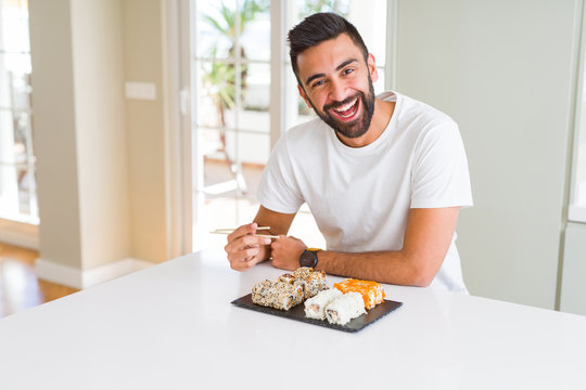 Handsome man smiling happy enjoying eating fresh colorful asian sushi using chopsticks