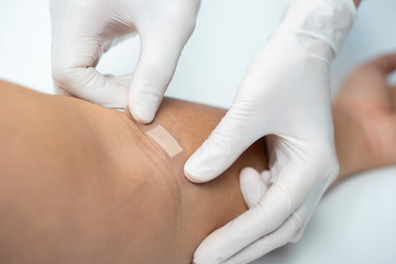 Close up nurse hand wearing white latex glove using wound plaster cover arm crook on white background. Skin bandage