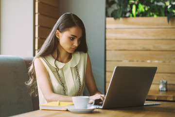 Beautiful girl working out a plan of the project and concept. Girl paints a website design on a laptop. student prints a message on the phone in the messenger. Development. Digital marketing