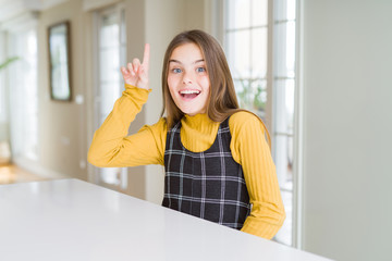 Beautiful young girl kid sitting on the table pointing finger up with successful idea. Exited and happy. Number one.