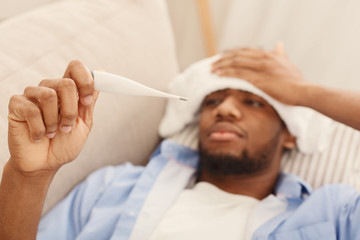 Sick black man checking his temperature at home