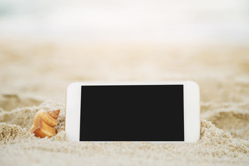 Mobile touch smart phone and shell on tropical sand at beach with bokeh sunlight water sea wave texture background. display screen black copy space of technology and travel nature concept. soft focus