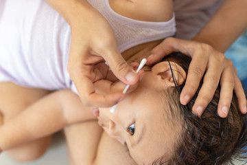 Obraz na płótnie Canvas Mother using cotton swab clean her baby's ear after bath.