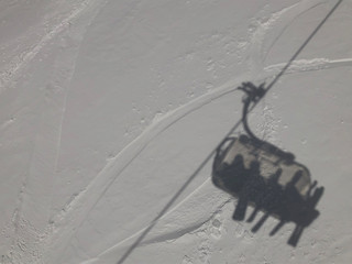 Shadow on snow of a ski slope, four people sitting on chairlift, skis and snowboards, take ride to get to the top of mountain, skier, vacation, sun, winter, resort, alps, San Domenico, Piedmont, Italy