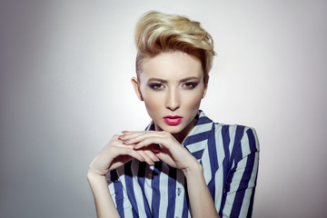 sensual woman wearing black swimsuit and striped shirt looking at camera while standing on grey background. indoor, studio shot on light grey background.