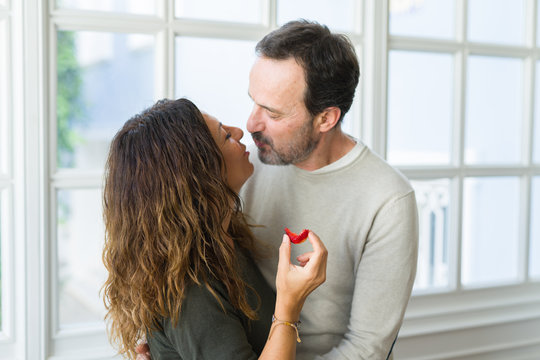 Middle age senior couple eating a fresh strawberry at home