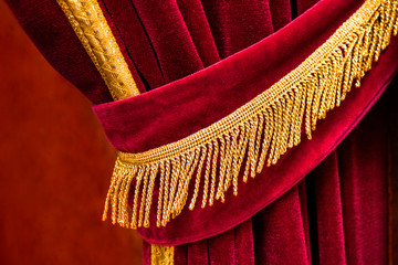 Close up detail of open and ruffeld red curtain with golden fringes tassel with blurred background...