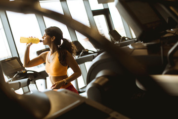 Young women in yellow sport shirt are drinking water at the gym