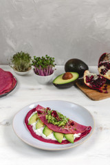 Tasty appetizing beetroot pancakes served on plate with avocado, sprouts and pink radish, white wooden table