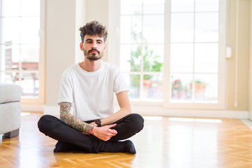 Young man working sitting casual on the floor at home with serious expression on face. Simple and natural looking at the camera.