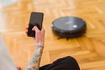 Close up of man hands controling automatic vacuum cleaner using electronic control of the mopping...