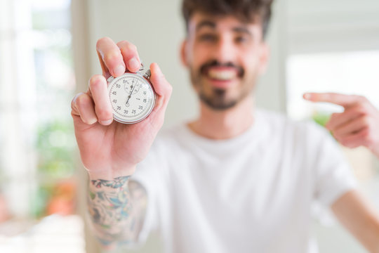 Young man using holding stopwatch very happy pointing with hand and finger