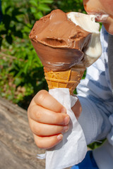 Cute child eating cone chocolate ice-cream in summer in a park. Little kid, little hand, no face, close up