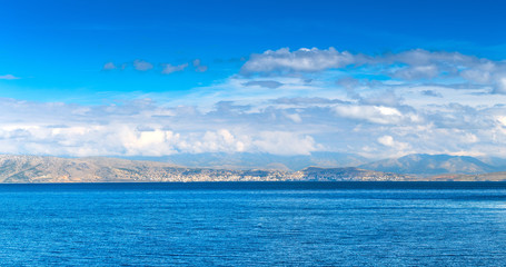 Obraz premium Beautiful summer panoramic seascape. Green slopes in close bays with crystal clear azure water. View on albanian city Saranda from north part Corfu island.