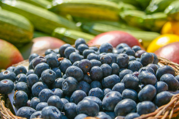 Fresh organic ripe blueberries in a basket with other blurred out of focus fruits and vegetables on the background, in a market, close up