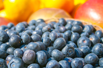 Fresh organic ripe blueberries in a basket with other blurred out of focus fruits and vegetables on the background, in a market, close up