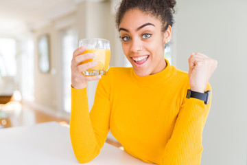 Young african american woman drinking a glass of fresh orange juice screaming proud and celebrating...