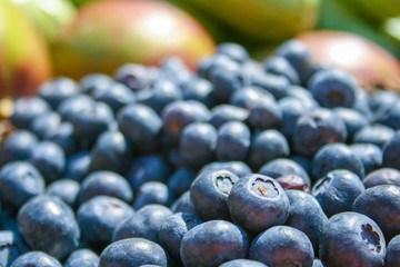 Fresh organic ripe blueberries in a basket with other blurred out of focus fruits and vegetables on the background, in a market, close up